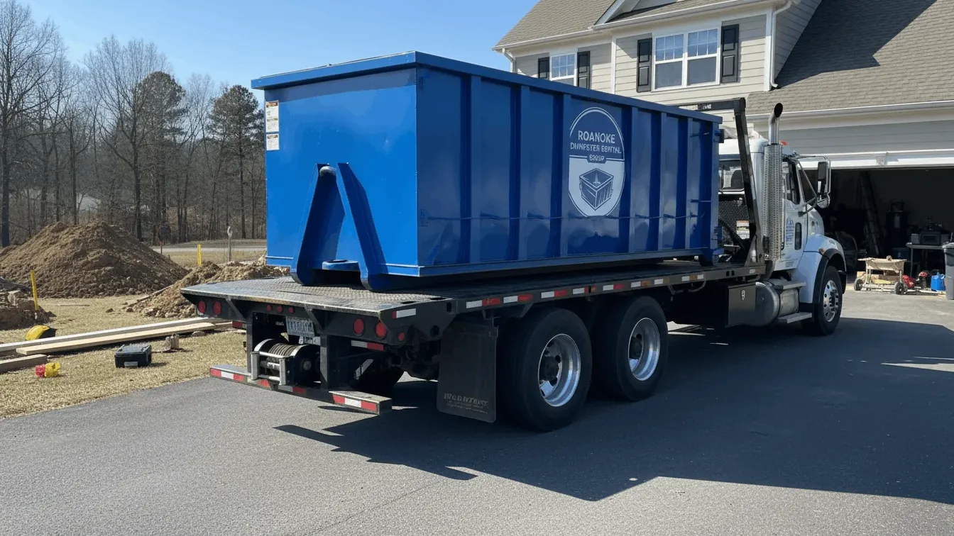 Commercial dumpster rental in Roanoke: a 30 yard roll-off backed to a loading dock off Williamson Road, traffic cones and reflective tape set out and flattened cardboard stacked against the wall before the driver drops the rails. Commercial dumpster rental in Roanoke: a 30 yard roll-off backed to a loading dock off Williamson Road, traffic cones and reflective tape set out and flattened cardboard stacked against the wall before the driver drops the rails.