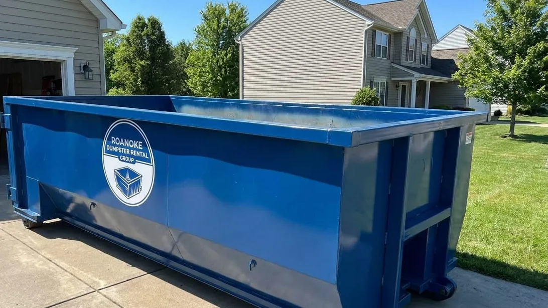 Residential dumpster rental in Roanoke: a 20 yard roll-off set on plywood down a sloping Raleigh Court driveway, crawlspace hatch open and rotted sill plate framing stacked flat across the floor of the container. Residential dumpster rental in Roanoke: a 20 yard roll-off set on plywood down a sloping Raleigh Court driveway, crawlspace hatch open and rotted sill plate framing stacked flat across the floor of the container.